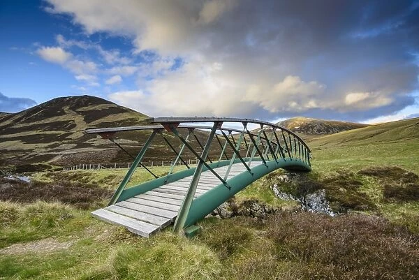 Metal footbridge over river in glen, in evening sunlight, Clunie Water, near Braemar, Cairngorms N. P