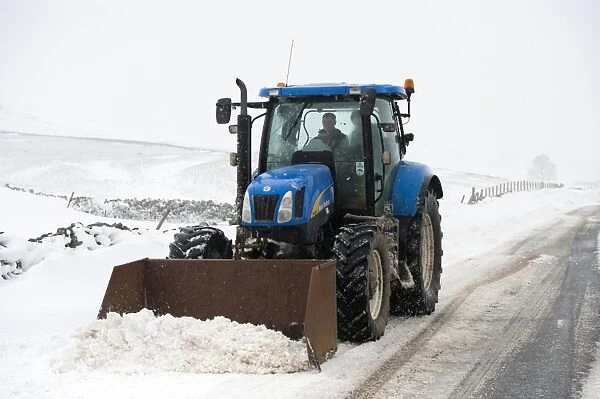 New Holland tractor clearing snow off rural road after snowstorm, Cumbria, England, March