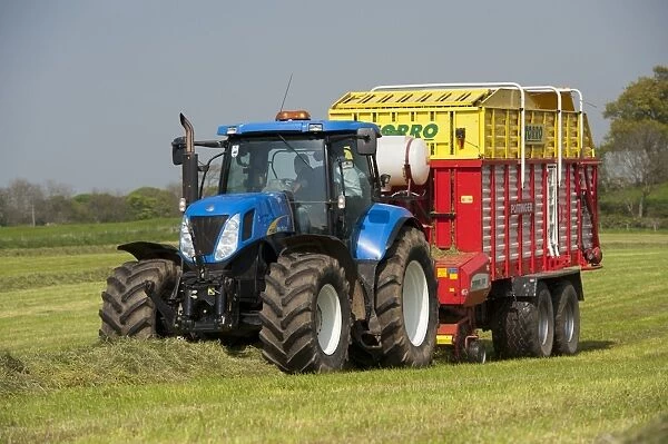 New Holland tractor with Pottinger forage wagon, picking up grass in silage field, Northumberland, England, May