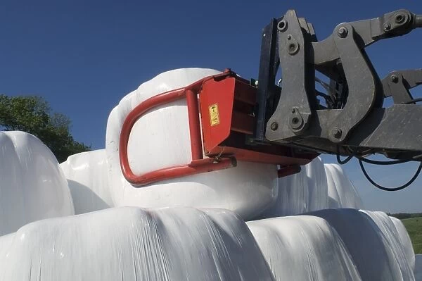 Plastic wrapped round silage bales, stacked onto pile with mechanical loader, Sweden