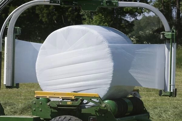 Plastic wrapping round silage bale with mechanical bale-wrapper, Sweden