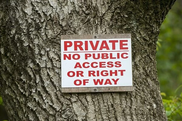 Private, No Public Access of Right of Way sign on tree trunk in woodland, Cumbria, England, May