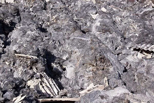 The remains of burnt straw bales after a Farm barn fire with bits of asbestos roofing mixed with the straw