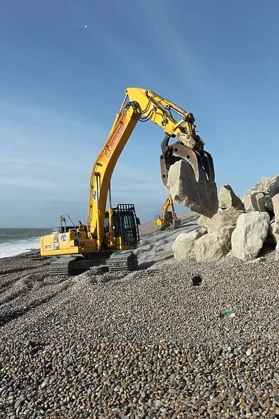 Repairing sea defences, excavator with grabber placing boulders on shingle beach, Chesil Beach, Dorset, England