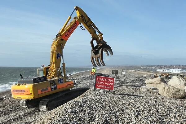 Repairing sea defences, excavator with grabber placing boulders on shingle beach, Chesil Beach, Dorset, England