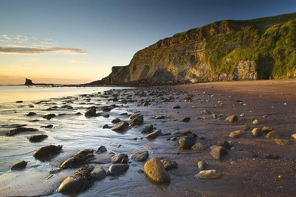 Rocks on sandy beach with sea cliffs at sunrise, Black Nab, Saltwick Bay, North Yorkshire, England, august