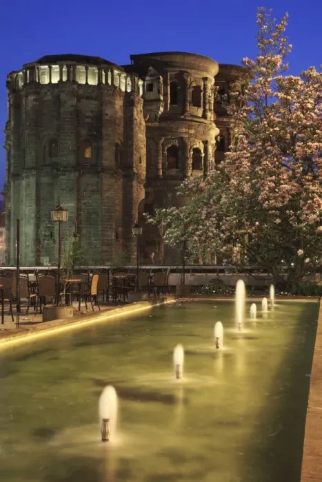 Framed Print : Roman city gate with fountains and flowering magnolia in foreground, illuminated at night, Porta Nigra, Trier