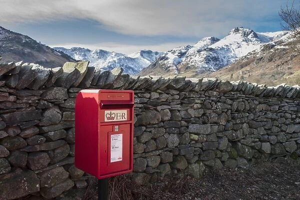 Royal Mail postbox beside drystone wall, with snow covered fell in background, Chapel Stile, Langdale