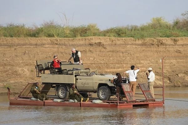 Safari vehicle and tourists crossing river on pontoon, River Luangwa, South Luangwa N. P. Zambia, June