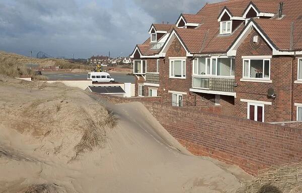 Sand blown from beach forming dunes building up against garden wall next to houses in seaside resort town, Lytham St. Anne's, Lancashire, England, january