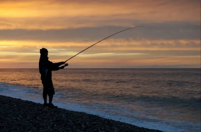 Framed Print : Sea angler fishing from shingle beach, silhouetted at sunset, Weybourne, Norfolk, England, august