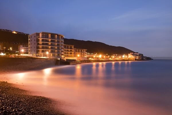 Sea rushing in over pebbles on beach below promenade in seaside resort before sunrise, Westward Ho