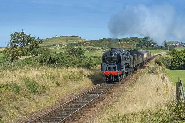 Steam train and carriages, passing through golfcourse with seaside town in background, North Norfolk Railway