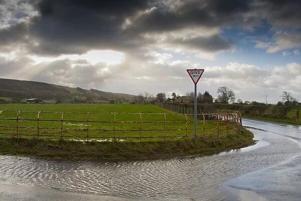 Stormclouds, Cheshire railings, Give Way sign and puddles on road, Thornley, Preston, Lancashire, England, december