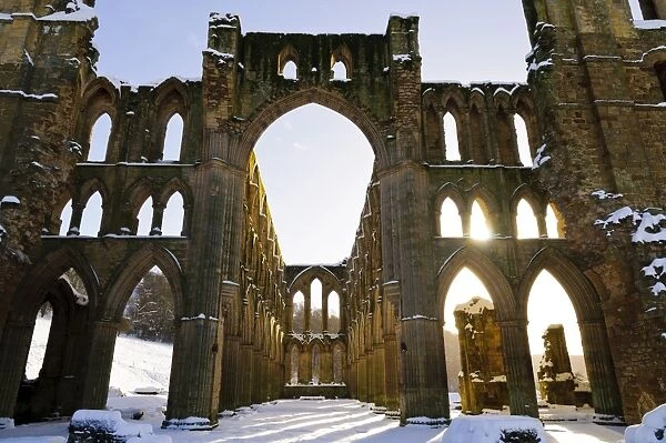 Sunlight shining through arched windows of ruined cistercian abbey in snow, Rievaulx Abbey, North York Moors N. P