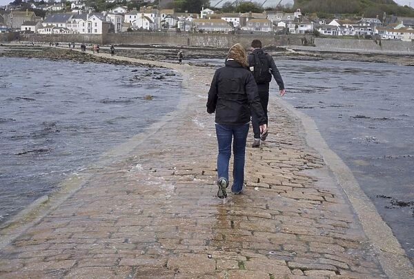 Tourists walking in seawater covering manmade causeway from tidal island, St