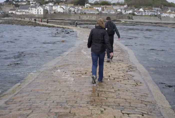 Framed Print : Tourists walking in seawater covering manmade causeway from tidal island, St