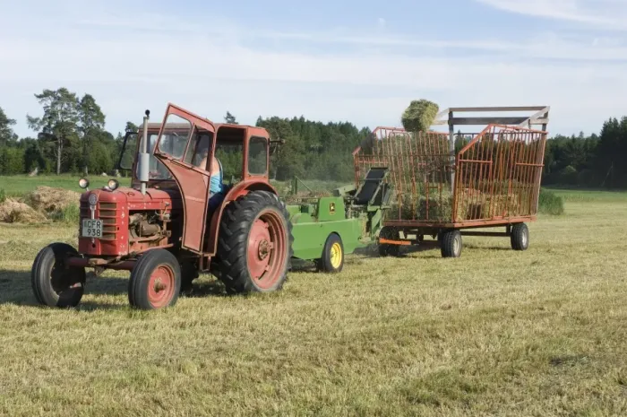 Framed Print : Tractor baling hay crop, baler tossing small bales into wagon, Sweden