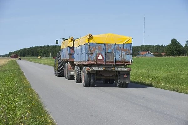 Tractor with covered trailers, transporting harvested grain on rural road, Sweden, august