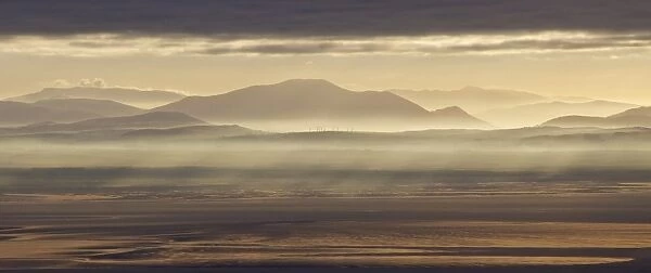 View across bay towards distant windfarm and hills at sunrise, looking towards Lake District (Cumbria, England)