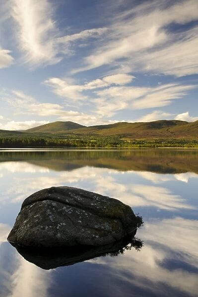 View of blue sky, clouds and rock reflected in still water of freshwater loch, Loch Garten, Abernethy Forest