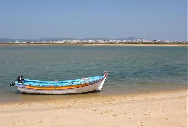 View of city from coastal island with fishing boat, Figo, Algarve, Portugal, april