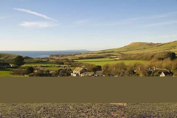 View over coastal farmland, with pasture, village houses and distant sea, Isle of Portland in distance, Kimmeridge