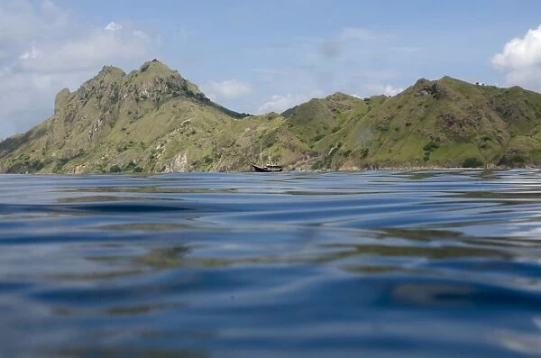 View of coastline with hills and ship from surface of sea, Mobula Point dive site, Padar Island, Komodo N. P