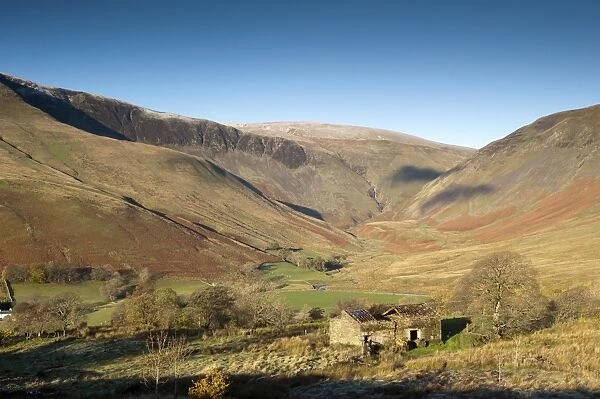 View of derelict barn and farmland in fell valley with waterfall in distance