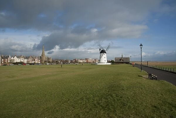 View of grass promenade in seaside resort town, with windmill and old lifeboat house in distance, Lytham Windmill