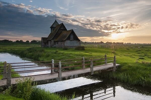 View of grazing marsh with footbridge across flooded ditch and church at sunset, St