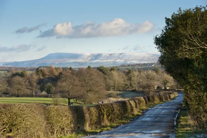 Framed Print : View of icy rural road, hedgerow and bare trees towards snow covered hill in distance, looking from Little Bowland Road toward Pendle Hill, Chipping, Lancashire, England, december
