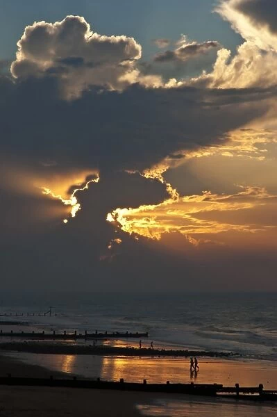 View of people on beach, groynes and clouds at sunset, Cromer, Norfolk, England, July