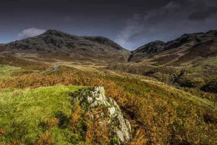 Framed Print : View of road snaking towards upland pass, with volcanic rock in foreground, Hardknott Pass, Lake District N. P