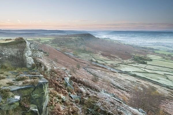 View of rocks and moorland across valley in frost at sunrise, looking from Curbar Edge towards Baslow Edge, Dark Peak