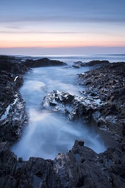 View of sea washing into large rockpool during incoming tide at sunset, Westward Ho!, North Devon, England, March