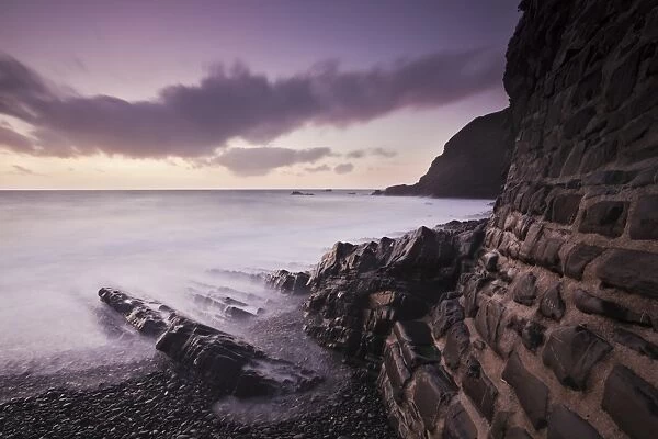 View of seawall, rocks on beach and cliff at sunset, Welcome Beach, North Devon, England, September