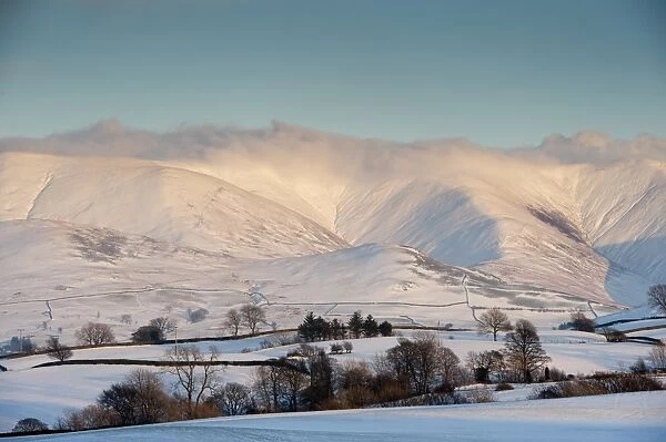 View of snow covered farmland and fells in evening sunlight, Howgill Fells, Cumbria, England, January