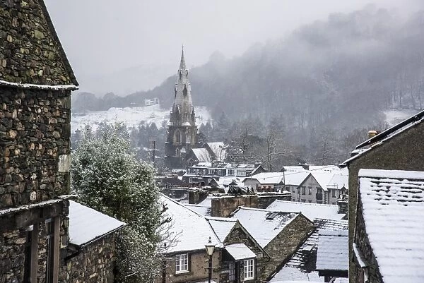 View across snow covered rooftops towards church spire in town, St. Marys Church, Ambleside, Lake District N. P