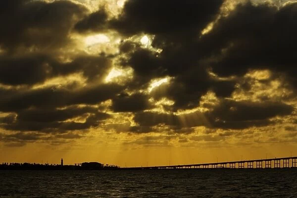 View of sunbeams over coast at sunset, with bridge to South Padre Island, Port Isabel, Texas, U. S. A. april