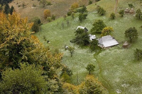 View of traditional farmland, with old houses, barns, fruit trees and pasture under light covering of snow in autumn