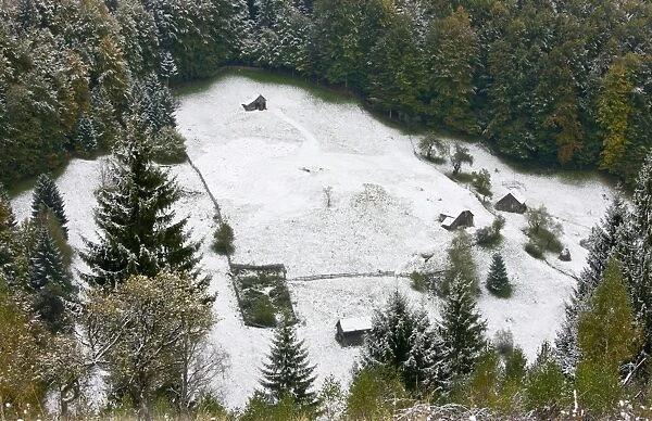 View of traditional farmland with small fields and barns, on mountain slopes covered with snow, Piatra Craiulu N. P