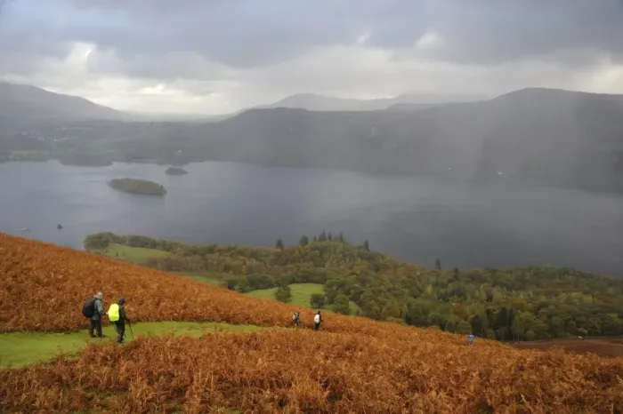 Framed Print : View of walkers descending through bracken covered fellside towards lake with rain squall overhead Framed Print : View of walkers descending through bracken covered fellside towards lake with rain squall overhead