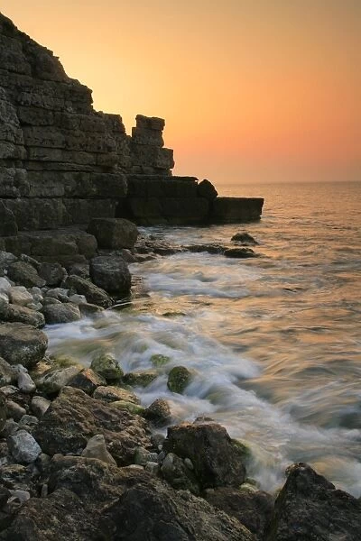View of waves on rocky beach and old quarry on cliffs at sunset, Winspit Bay, near Worth Matravers, Isle of Purbeck