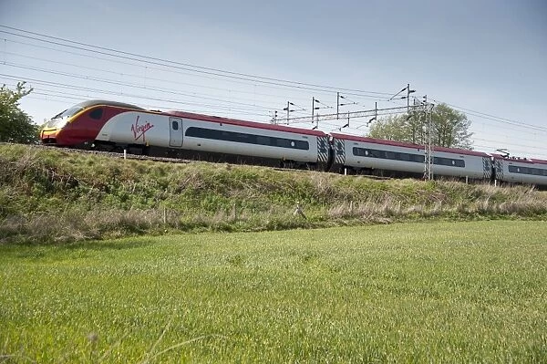 Virgin railway train travelling along bank in farmland, Wrinehill, Staffordshire, England, may