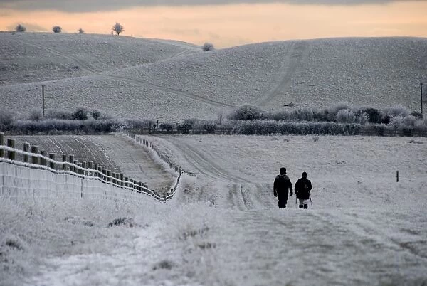 Walkers on frost and snow covered footpath at sunset, Ridgeway Path, near Pitstone Hill, Chilterns, Buckinghamshire
