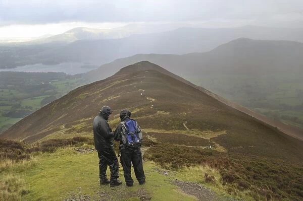 Walkers wearing waterproof clothing, looking at map during rain shower, view from Causey Pike