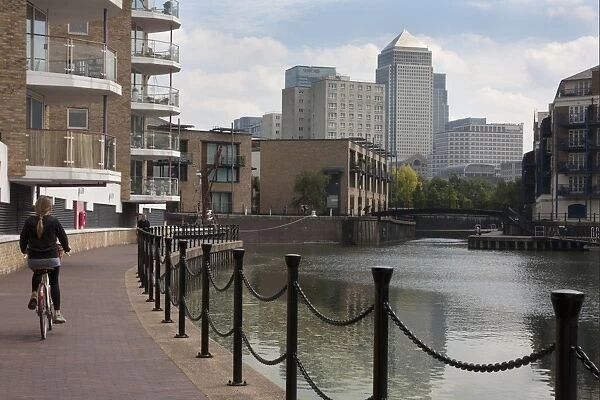 Woman cycling beside waterway with redevelopment, Canary Wharf in distance, Limehouse Basin, Limehouse, Tower Hamlets