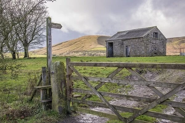 Wooden public footpath sign and stile beside gate, with stone out-barn in field, Chipping, Lancashire, England