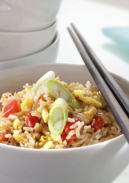 Bowl of egg-fried rice with red bell peppers and celery, with chopsticks resting on top, and a stack of bowls nearby, close-up